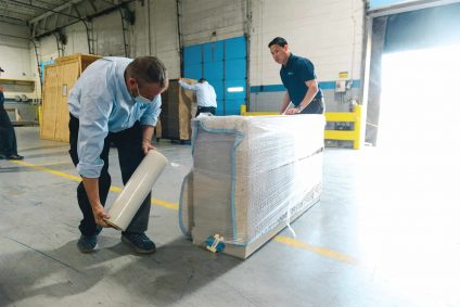 Blue Kangaroo Packoutz associates packing an item in shrink wrap
