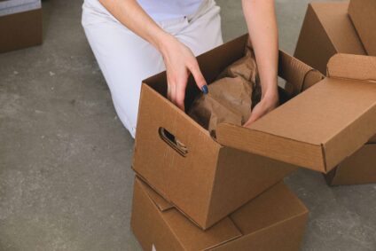 a woman's hands packing belongings into a cardboard box.