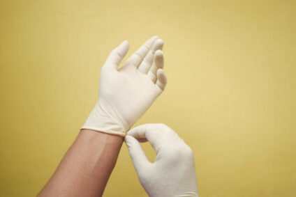 a pair of hands wearing white gloves against a yellow background.
